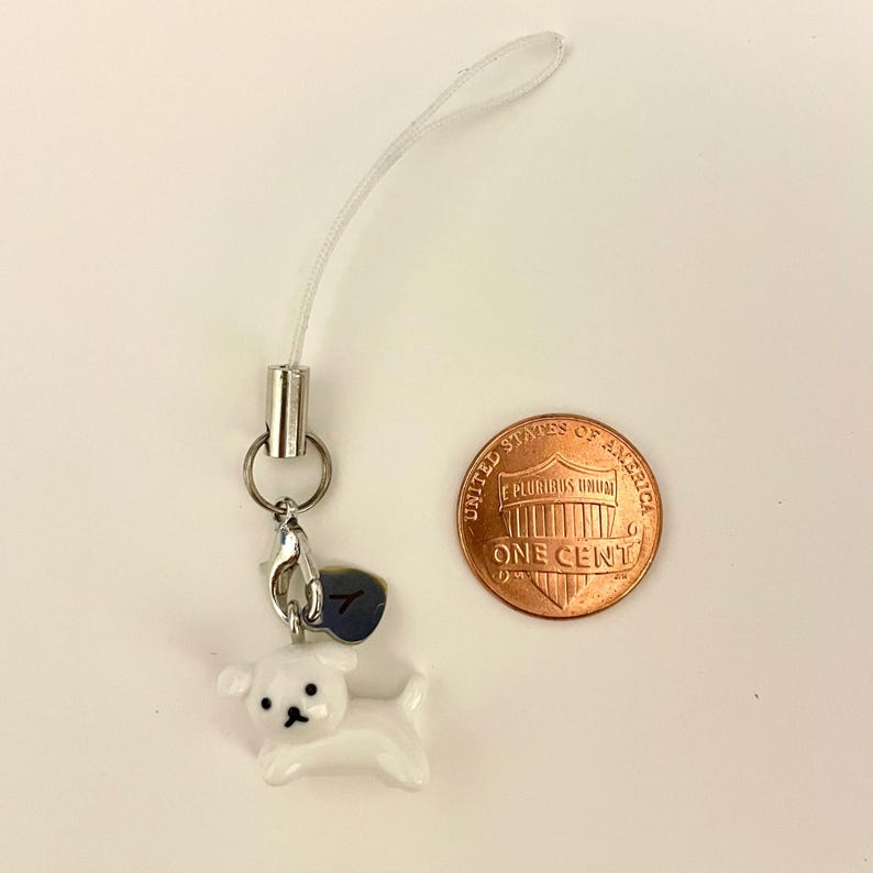 May include: White ceramic dog charm with a silver clip and a silver charm with the number 7 on it. The charm is attached to a white string.