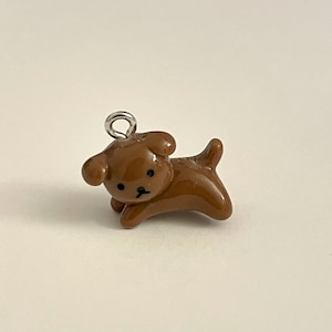 May include: A brown ceramic dog charm with a silver loop for hanging. The dog has black eyes and a small black nose.