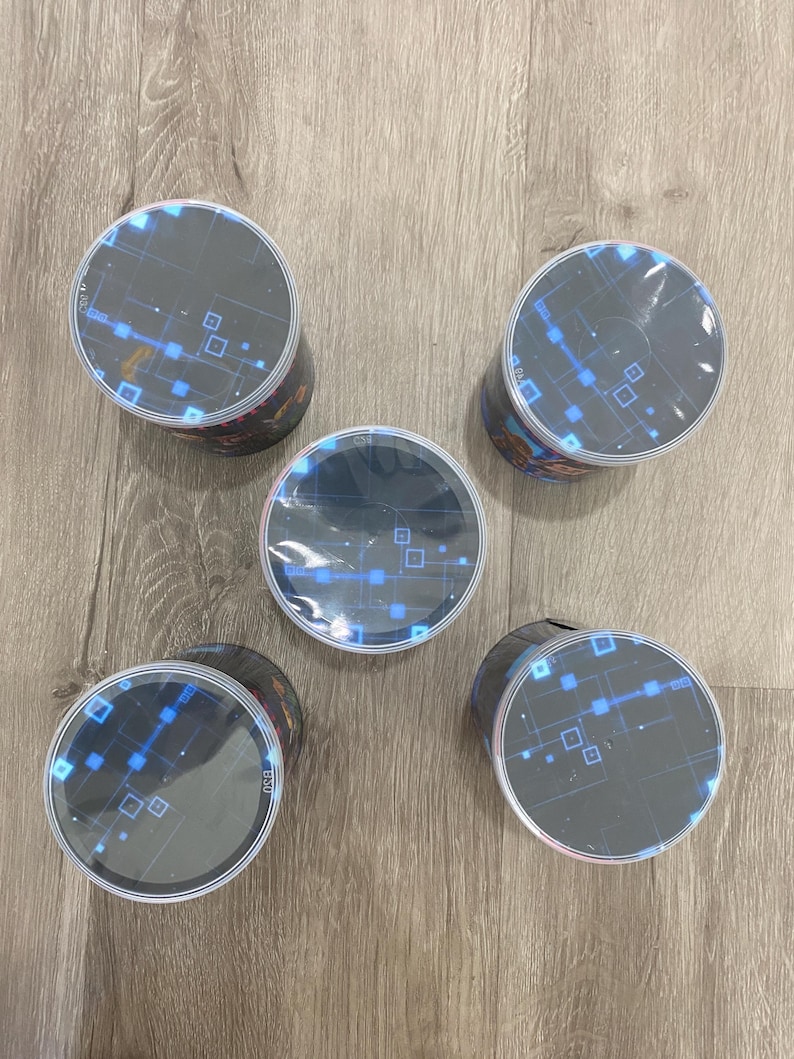 May include: Five cylindrical containers with black sides and clear, circular tops. The tops feature a blue and white digital design with squares and lines. The containers are arranged on a light wood-grain surface.