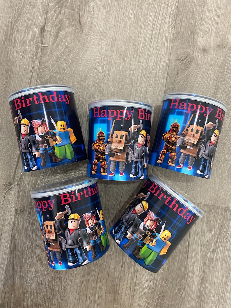 Puede incluir: Cinco recipientes cilíndricos con fondo azul y las palabras "Happy Birthday" en rosa. Cada recipiente presenta una ilustración de dibujos animados de personajes con herramientas. Los recipientes son probablemente para regalos de fiesta.