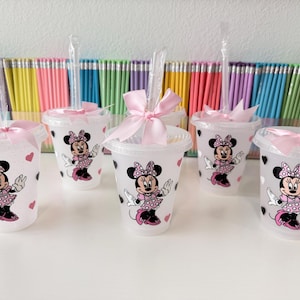 May include: Five translucent plastic cold cups with lids and clear straws, each decorated with a Minnie Mouse graphic wearing a pink polka dot dress. Each cup features a light pink satin ribbon bow tied around the straw and small heart accents.