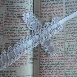 May include: A white crocheted lace bookmark with a white satin ribbon. The bookmark is placed on an open Bible with text about Jesus. The text reads, "All things are possible with God."