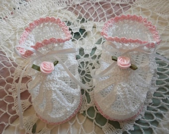 May include: A pair of white crocheted baby booties with pink trim and a pink satin rose on each bootie.