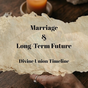 May include: A lit orange candle sits on a wooden surface near a torn paper with the words "Marriage & Long-Term Future Divine Union Timeline". A hand with a ring is visible.