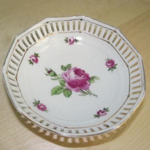 May include: A white porcelain dish with a gold rim and a delicate openwork design. The dish is decorated with pink roses and green leaves.