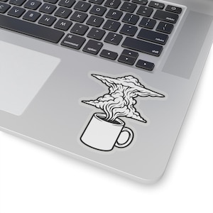 May include: A white sticker featuring a coffee mug with steam rising to form a cloud shape. The sticker is placed on a silver laptop, with the keyboard visible in the background.