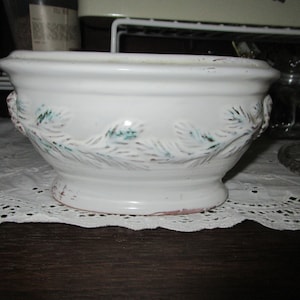 May include: White ceramic bowl with a green and brown leafy design around the rim. The bowl has a slightly rounded base.