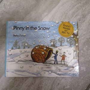 May include: A children's book titled "Pinny in the Snow" by Peter Firmin. The cover features a colorful illustration of a snail in the snow with two children standing next to it. A yellow circle with the text "Pinny's House on BBC TV" is in the upper right corner.