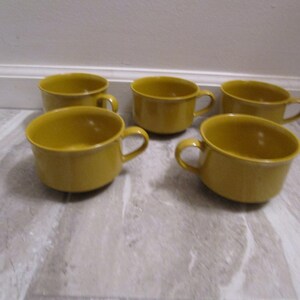 May include: Five yellow ceramic mugs with handles. The mugs are all the same size and shape.
