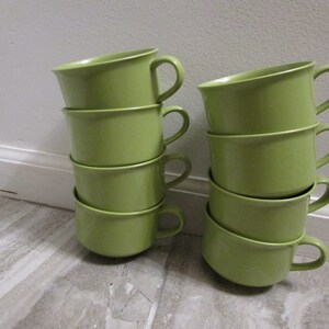 May include: A stack of six green ceramic mugs with rounded handles. The mugs are stacked in two groups of three.