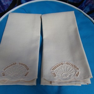 May include: Two off-white linen tea towels with scalloped edges and embroidered floral designs.