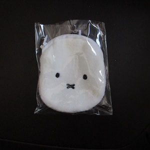 May include: A white plush coin purse in a clear plastic package. The purse is round with black eyes and a black cross-shaped mouth. The purse is designed to look like a cartoon character.