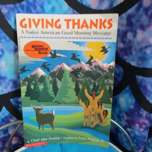 May include: A children's book titled "Giving Thanks: A Native American Good Morning Message" with an illustration of a mountain landscape, a deer, and Native American people. The book is part of the "Reading Rainbow Book" series.