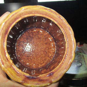 May include: A ceramic jar with a scalloped rim, in shades of brown and yellow. The interior is a darker brown with a textured surface. The jar's design suggests it could be used for storage or display.