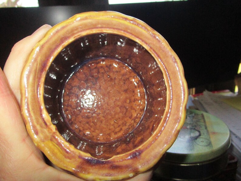May include: A ceramic jar with a scalloped rim, in shades of brown and yellow. The interior is a darker brown with a textured surface. The jar's design suggests it could be used for storage or display.