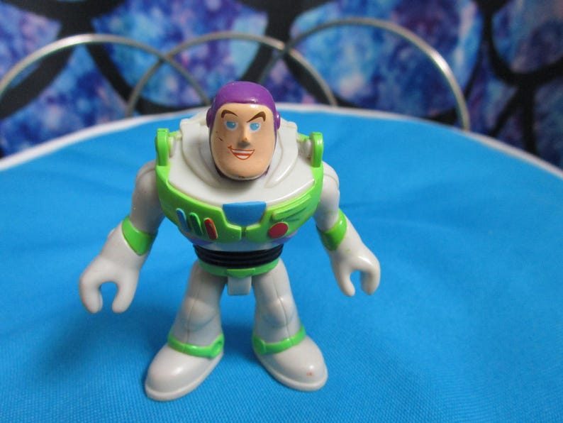 May include: A Buzz Lightyear action figure, featuring a white and green spacesuit with purple accents. The toy has a smiling face and is posed on a blue surface. The figure is a collectible toy.