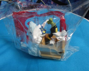 May include: A plastic toy set featuring a white and blue character with a black mask and a black and green character with a yellow hat. The characters are sitting in a brown boat with a red and white sail. The toy is packaged in a clear plastic bag.
