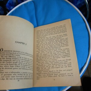 May include: A close-up of an open book with the title "Overdrive" and the chapter title "Chapter 2". The book is open to a page with text about a spaceship and the crew members. The book is on a blue surface.