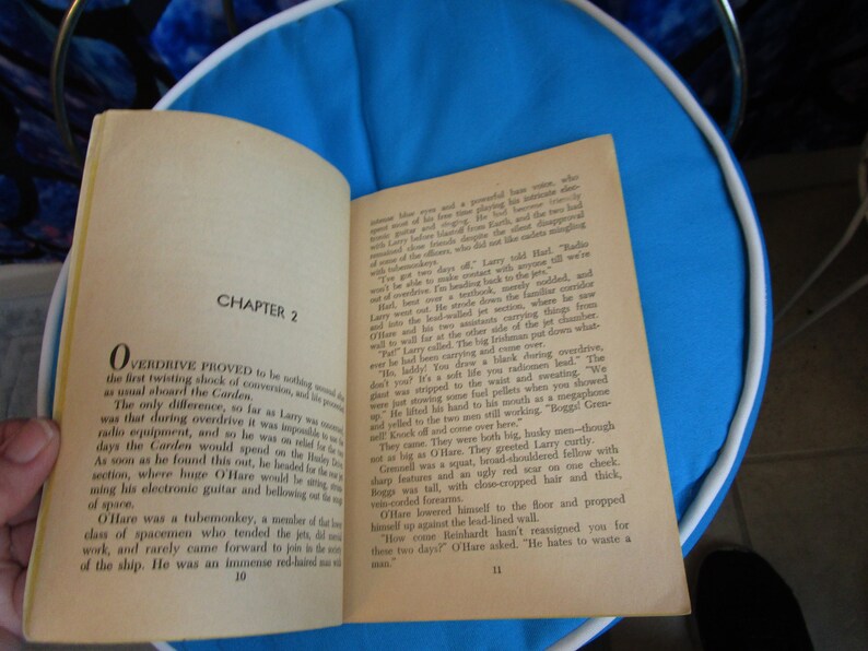 May include: A close-up of an open book with the title "Overdrive" and the chapter title "Chapter 2". The book is open to a page with text about a spaceship and the crew members. The book is on a blue surface.