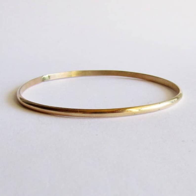 Puede incluir: Un brazalete de oro simple. El brazalete es delgado y tiene un acabado liso y pulido.