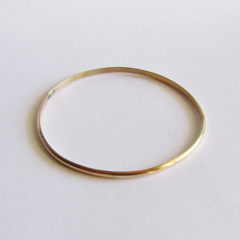 Puede incluir: Un brazalete de oro simple. El brazalete es delgado y tiene un acabado liso y pulido.