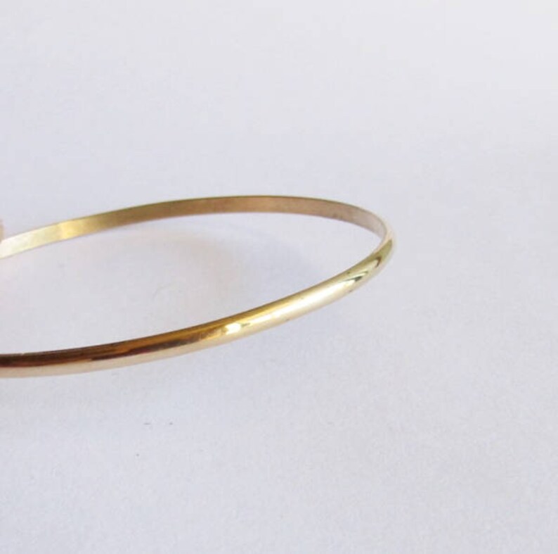 Puede incluir: Un brazalete de oro simple. El brazalete es delgado y tiene un acabado liso y pulido.