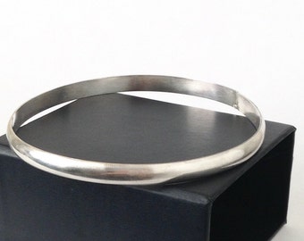 May include: A silver bangle bracelet with a smooth, polished finish. The bracelet is displayed on a black box.