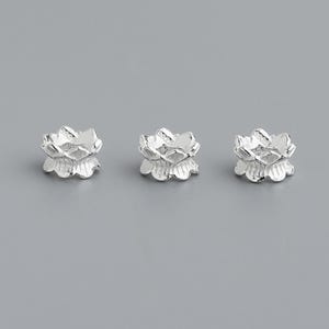 Puede incluir: Tres abalorios de plata con forma de flor de loto. Los abalorios son peque&ntilde;os y delicados, con un dise&ntilde;o detallado.