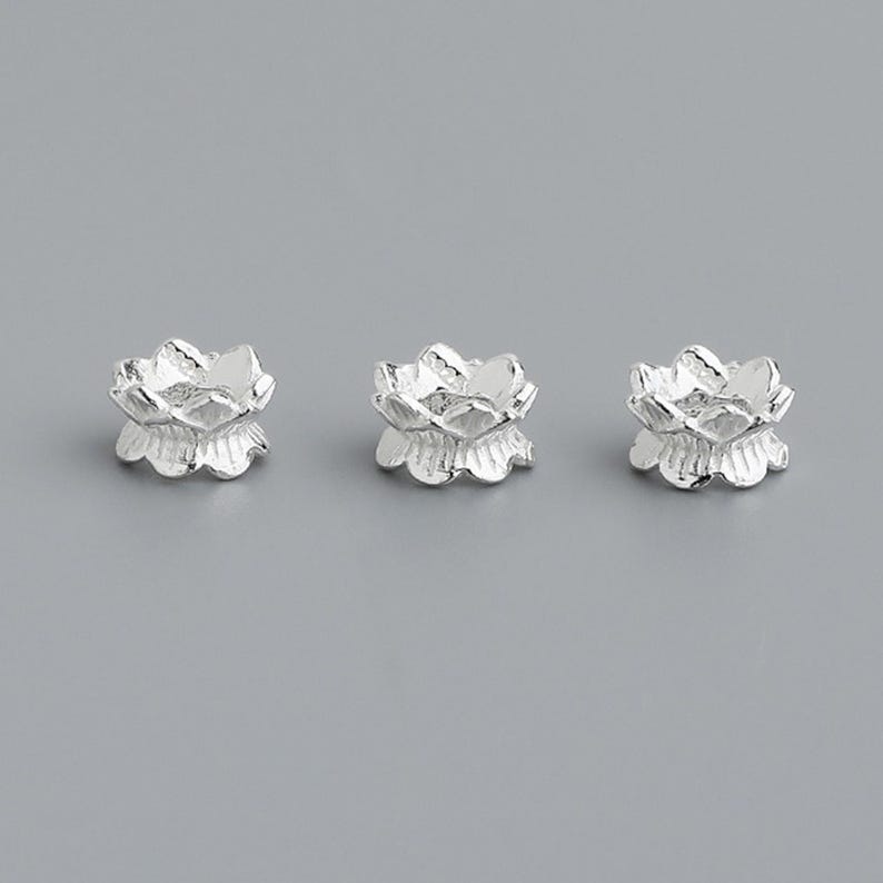 Puede incluir: Tres abalorios de plata con forma de flor de loto. Los abalorios son peque&ntilde;os y delicados, con un dise&ntilde;o detallado.