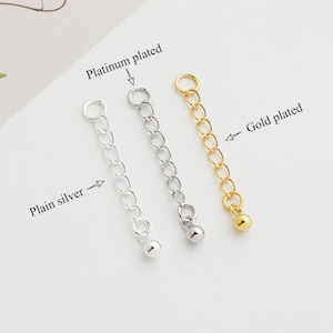 May include: Three silver chains with a ball at the end. The chains are labeled "Plain silver", "Platinum plated", and "Gold plated".