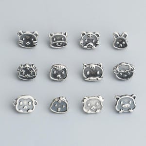 May include: A collection of twelve silver-colored animal-faced beads. The beads feature various animals, including a mouse, tiger, rabbit, hedgehog, monkey, dog, and pig. Each bead has a detailed, cartoon-like design.