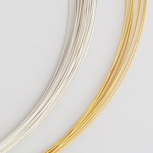 May include: Close-up of silver and gold craft wire. The silver wire is on the left, and the gold wire is on the right. The wires are thin and appear to be made of metal. The background is white.