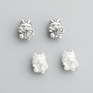 May include: Four small, silver-colored figurines of a mythical creature, each holding a rectangular object with Asian characters. The figurines have detailed features and are arranged on a gray background.
