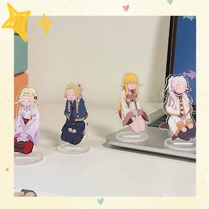 Puede incluir: Cuatro soportes acrílicos de personajes de estilo anime. Cada soporte presenta un personaje diferente con cabello largo y ropa detallada. Los personajes están en varias poses, con una base transparente para exhibir. El fondo incluye una computadora portátil y una superficie de color claro.