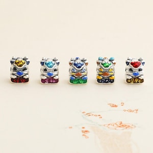 May include: Five silver-toned, rectangular beads with colorful enamel designs. Each bead features a stylized animal face with blue, yellow, and red accents. The bottom of each bead has a different color and Chinese characters. These beads are likely for jewelry making.