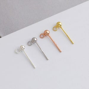 May include: Four stud earrings in silver, silver-tone, rose gold, and gold. Each earring features a small ball at the top and a post with a loop for attaching a backing. The earrings are displayed on a white surface.