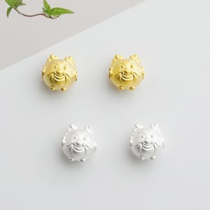May include: Four small, round, smiling face charms. Two are gold-colored, and two are silver-colored. The charms have a cartoon-like design with eyes, a nose, and a smiling mouth. The background is white.