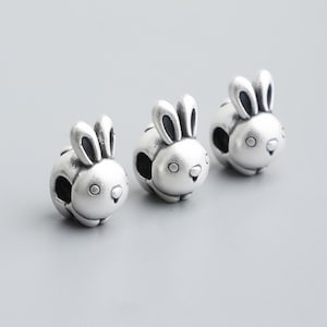 May include: Three silver-colored bunny charms with black accents. Each charm features a round body, large ears, and a small face. The charms are designed to be used as beads or pendants for jewelry making.