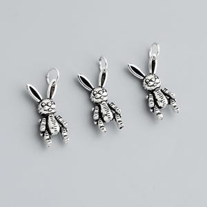 May include: Three silver-colored bunny charms with detailed features, including long ears and textured bodies. Each charm has a small loop at the top for attaching to a chain or bracelet. The charms are displayed against a gray background.