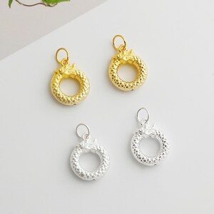May include: Four pendant charms in gold and silver. Each charm features a circular design with a dragon head at the top. The gold charms have a shiny finish, while the silver charms have a matte finish. These charms are suitable for jewelry making.