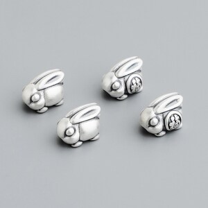May include: Four small, silver-colored rabbit charms. Each charm has a detailed bunny shape with long ears and a small, round body. The charms are on a gray background.
