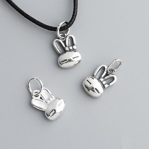 May include: Silver-toned bunny pendant charms. The charms feature a bunny face design with large ears and a small loop for attaching to a necklace or bracelet. One charm is on a black cord.