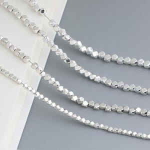 May include: A close-up of four strands of silver beads. The beads are faceted and have a geometric shape. The beads are strung on a clear thread.