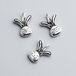 May include: Three silver-colored bunny charms. Each charm features a rabbit head with long ears and detailed facial features. The charms are small and appear to be made of metal, possibly for jewelry making or crafting.