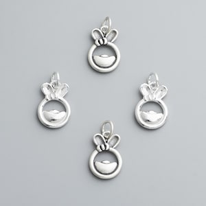 May include: Four silver-colored charms with a bunny ear design above a circular frame. The frame holds a curved, boat-shaped element. Each charm has a small loop at the top for attachment. The charms are displayed on a gray background.