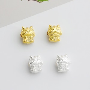 May include: Four small, detailed figurines in a symmetrical arrangement. Two are gold-colored, and two are silver-colored. Each figurine depicts a stylized creature with a smiling face and intricate details, possibly for jewelry or decorative use.