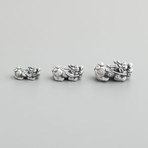 May include: Three silver charms in the shape of a mythical lion, each with intricate details and a circular design on the chest. The charms are different sizes, with the largest charm in the centre and the smallest charm on the left.