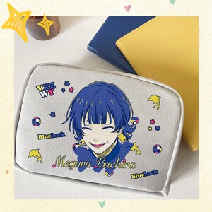 Puede incluir: Un neceser gris claro con un personaje de anime de pelo azul y el nombre "Meguru Bachira". La bolsa está decorada con estrellas, delfines y el texto "Blue Lock".