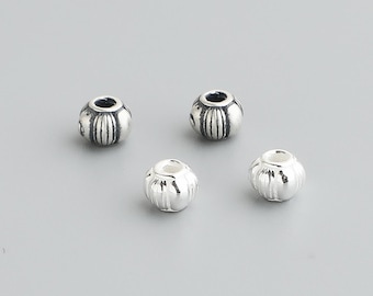 May include: Four small, silver-colored beads with a ribbed design. Each bead has a cylindrical shape with vertical grooves and a hole running through the center. The beads are displayed against a gray background.