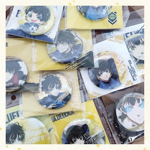 May include: A collection of anime-themed pinback buttons featuring various characters. The buttons are round with colorful illustrations and text, packaged on cardboard backing. The overall color scheme includes blue, yellow, and white.